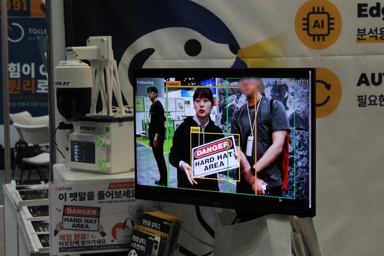 AUTO PTZ 시연 화면. 'DANGER HARD HAT AREA' 팻말을 든 사람을 인식해 추적하는 모니터와 LOOKAT 장비